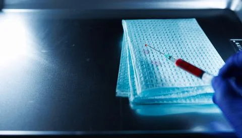 Close-up of a hypodermic needle with a drop of blood at the tip being held .. Stock Photos