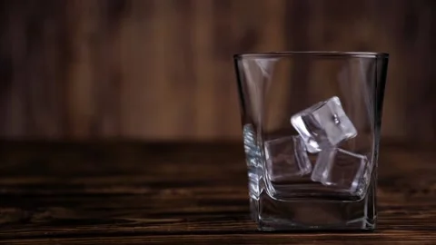Close-up of ice cubes falling into an empty glass on a dark wooden background Stock Footage 130464217