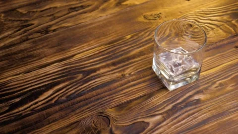 Close-up of ice cubes falling into an empty glass on a dark wooden background Stock Footage 130823896