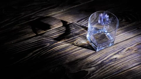 Close-up of ice cubes falling into an empty glass on a dark wooden background. Stock Footage 131947413