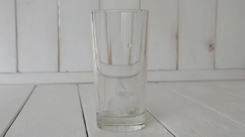 Close-up of ice cubes falling into an empty glass on a light wooden background. Stock Footage 145134223