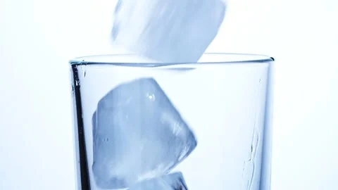 Close-up of ice cubes falling into an empty transparent glass Stock Footage 147353475