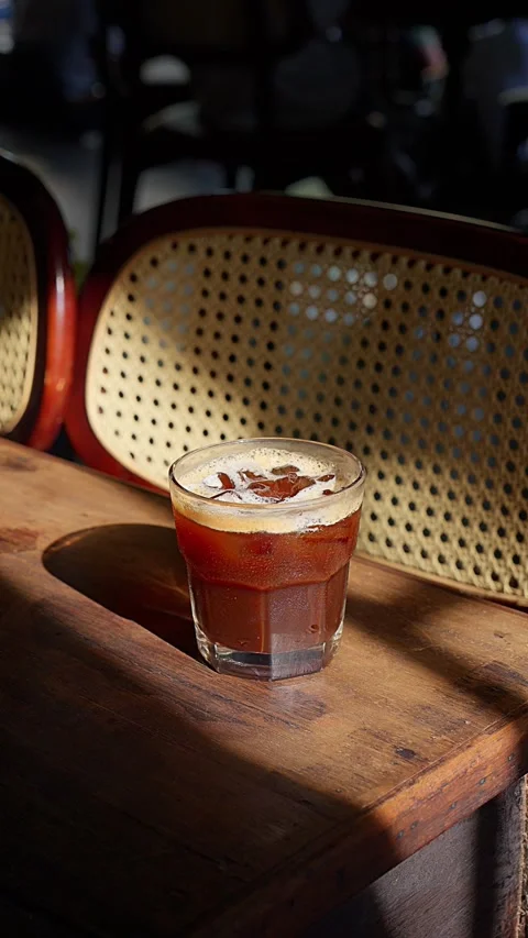 Close up iced brown coffee on an old wooden table in a sunbeam 스톡 동영상 343629487