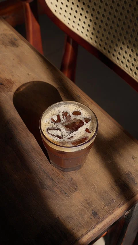 Close up iced brown coffee on an old wooden table in a sunbeam 스톡 동영상 343629574