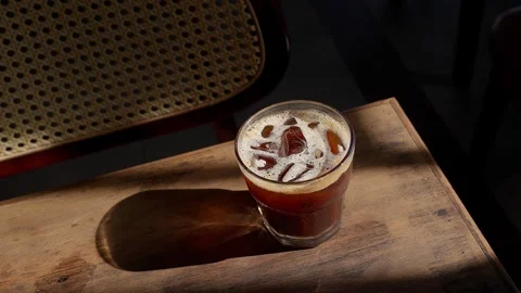 Close up iced brown coffee on an old wooden table in a sunbeam 스톡 동영상 343629640