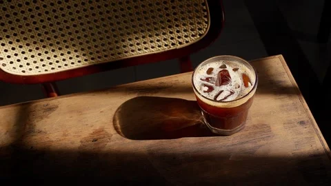 Close up iced brown coffee on an old wooden table in a sunbeam 스톡 동영상 343629692