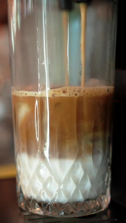 Close-up of iced coffee blending with cold milk in a tall textured glass Stock Footage 346719424