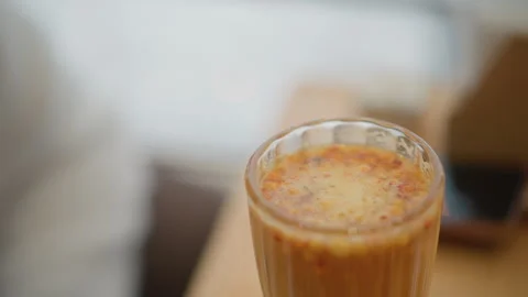 Close-up iced coffee glass with frothy crema and surface ripples on wooden table Stock Footage 346633723