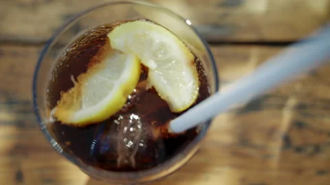 Close up of iced cola drink with lemon slices being mixed with a white straw in Stock Footage 337200276