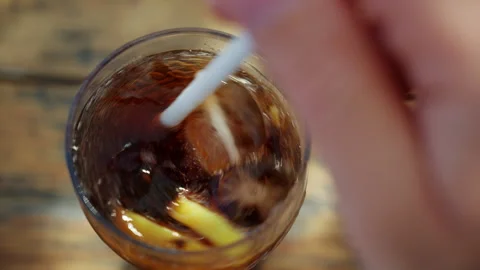 Close up of iced cola drink with lemon slices being mixed with a white straw in Stock Footage 337200701