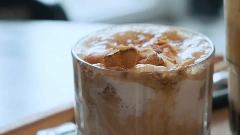 Close up of iced creamy coffee topped with caramelized chunks and foam in glass Stock Footage 312813962