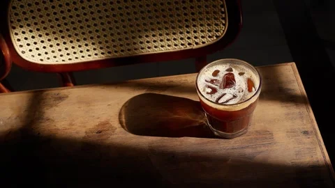 Close up iced dark brown coffee resting on old wooden table in beautiful window Stock Footage 345630219