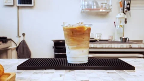 Close-up of iced latte in a plastic cup stir with green stick on a cafe counter Stock Footage 314501393
