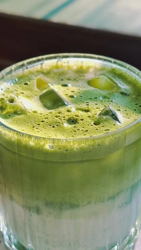 Close-up of an iced matcha latte with ice cubes and creamy foam in a glass Vídeos de archivo 340439391