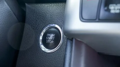 Close up of illuminated engine start stop button with chrome trim beside dark 스톡 사진