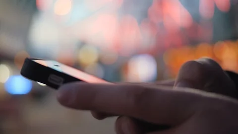 Close-up image of a child's hands using a smartphone at night on a city shopping Stockbeeldmateriaal 93363760