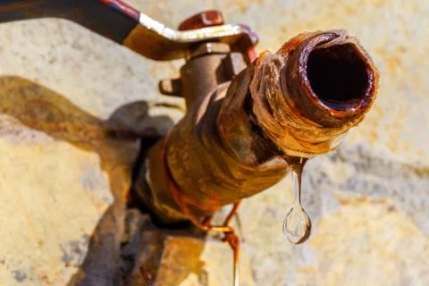Close up image of a drop of water dripping from a rusty tap. Stock Photos