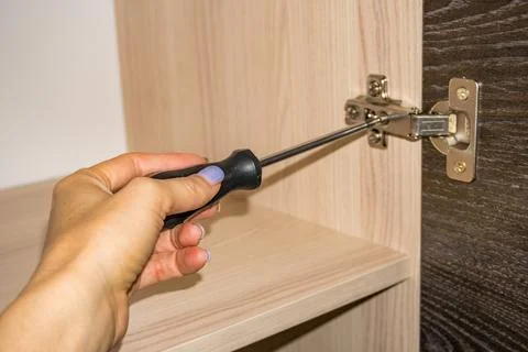 Close-up image of handyman assembling kitchen cabinet and screwing door hinge Stock Photos