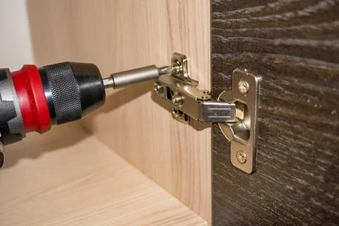 Close-up image of handyman assembling kitchen cabinet and screwing door hinge Stock Photos