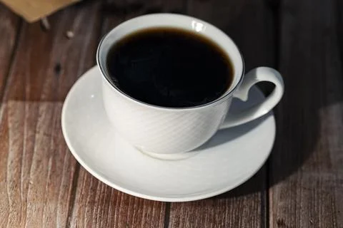 A close-up image of hot coffee in a white mug, with bread on a table, in th.. Stock Photos