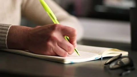 Close up image of human holding pen and writing something on blank white page Stock Footage 311190175