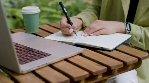 Close-up image of a lady sitting at the table writing in a notebook and at the Stock Footage 209589995