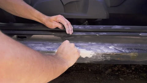 Close-up image of a man sanding and removing paint on the side of a car with a Stock Footage 278312592