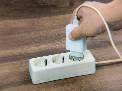 Close-up image of a man's hand trying to plug a cell phone charger to the e.. Fotos de archivo