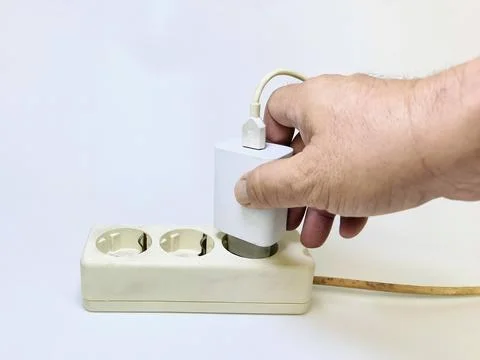 Close-up image of a man's hand trying to plug a cell phone charger into an .. Fotos de archivo