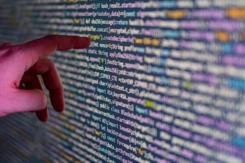 A close-up image of a persons hand pointing at a code display on a large scre Stock Photos
