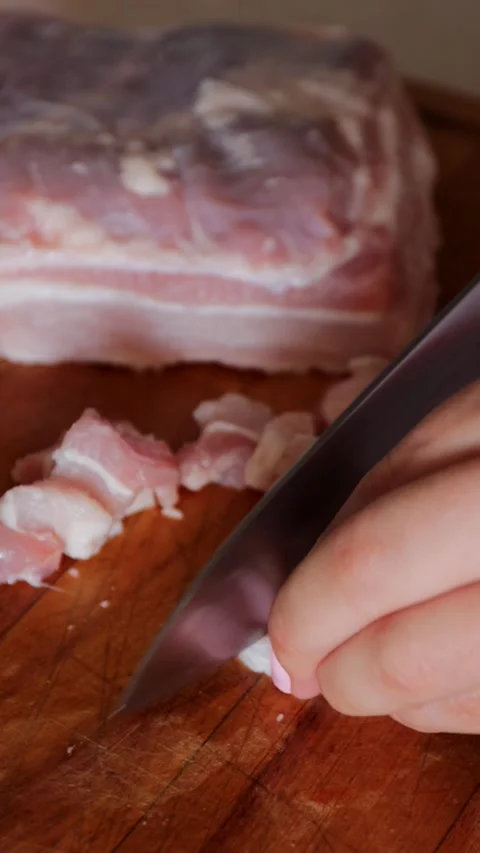 A close-up image of raw bacon being sliced into small chunks on a wooden cutting Stock Footage 314267034