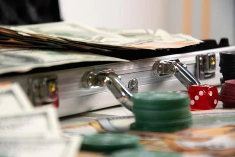 A close-up image of a silver suitcase open on a table with cash, a red dice.. Stock Photos