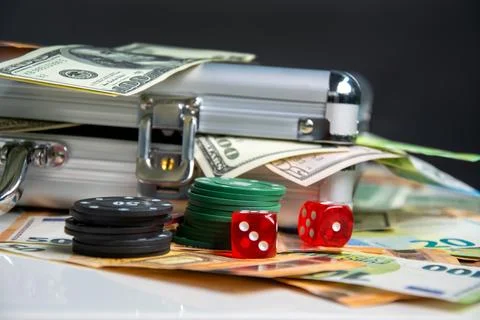 A close-up image of a table with stacks of cash, poker chips, and dice, sug.. Stock Photos