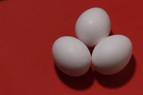 Close-up image of three chicken white eggs on a red background. Stock Photos