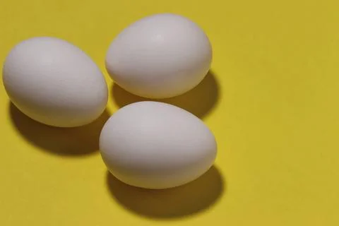 Close-up image of three chicken white eggs on a yellow background. Stock Photos