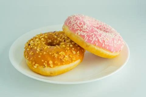 Close-up image of three donuts on a white plate against a light gray backgrou Stock Photos