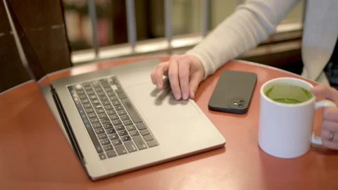 Close-up image of a woman's hands as she works on a laptop, with a cup of gre Video stock 275279452