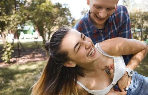 Close up image of young couple having fun and laughing in park. Boyfriend hugs Stock Photos