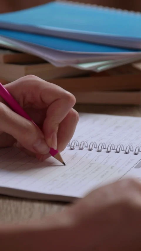 Close-up image of a young woman's hand taking notes and writing with a pencil in Stock Footage 305408182
