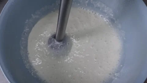 Close-up of an immersion blender mixing a light, bubbly liquid in a blue bowl Vídeos de archivo 335041248