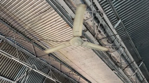 Close up of industrial ceiling fan spinning beneath corrugated metal roof Stock Footage 340975637
