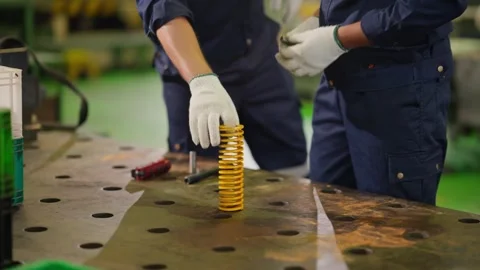 Close Up of Industrial Worker Picking Up Yellow Coil Spring from Table Stock Footage 343428905