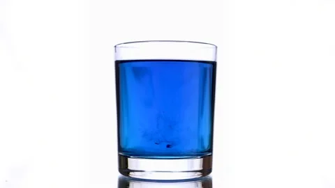 Close-up of an ink drops splashes into a glass of blue colored water. Stock Footage 154434043