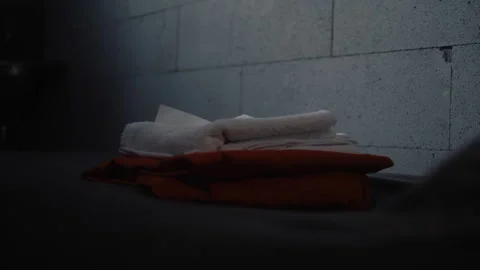 Close up of inmate placing orange prison uniform and bathroom accessories on bed 스톡 동영상 268567737