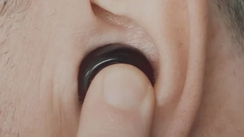 Close-up of inserting a black Bluetooth earphone into the ear and turning it  Stock Footage 302163079