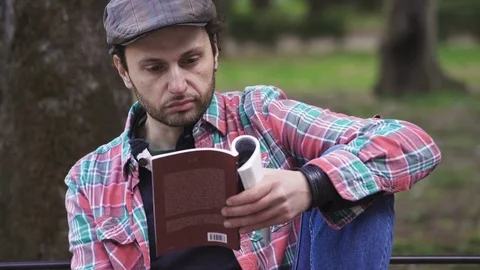 Close up on intellectual young man reading book  sitting at park Video stock 74706218