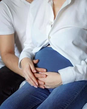 Close-up of the interlinked hands of a loving couple resting on a pregnant wife' Stock Photos