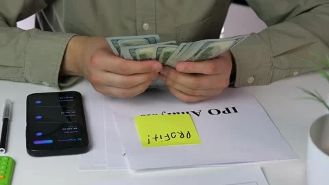 Close-up of an investor counting profits while referring to IPO analytics and a Video stock 316584737