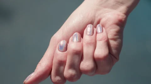 Close up iridescent nails on interlaced fingers with soft focus background Stock Footage 345134099