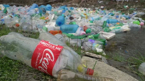 CLOSE UP: Ironic shot of plastic Coca Cola bottle with waste pollution at river Stock Footage 195024149